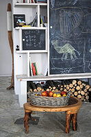 Rustikaler Holzhocker mit Obstkorb vor einem Regal mit Tafelwand