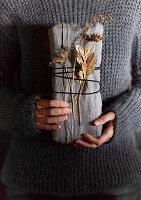 Linen-wrapped gift with string and dried flowers, held by person in knitted sweater