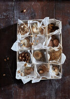 Cones, walnuts and Christmas baubles in a box with compartments on a wooden base
