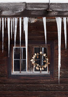 Rustic wooden hut with icicles and golden wreath of leaves on the window