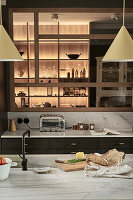 Moderne Küche mit beleuchteten Regalen, Arbeitsplatten aus Marmor und Hängeleuchten
