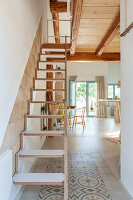 Folding wooden staircase in modern living room with patterned tiled floor and wooden beamed ceiling