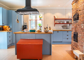 Kitchen with blue cupboards, wooden chest in rust red and brick wall with oven