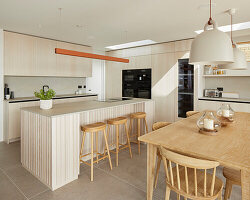 Moderne Küche mit Kochinsel, Barhockern aus Holz und Esstisch, Strandhaus-Stil
