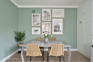 Essbereich mit Rattan-Stühlen und Bildergalerie an mintgrüner Wand