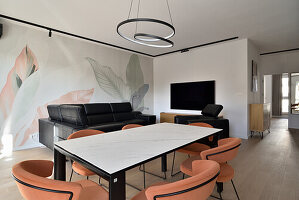 Living room with mural, black leather sofa and marble table with orange-colored chairs