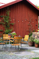 Garden seating area with wooden chairs and potted plants in front of red wooden house