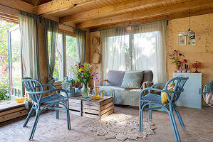 Sommerliches Gartenhaus mit blauen Rattanstühlen, Holztisch und Blumenstrauß