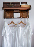 Wooden wardrobe with vintage suitcase on hat shelf and white dresses on wooden hangers