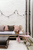 Seating area on terrace with rattan bench, patterned cushions and pink tricycle