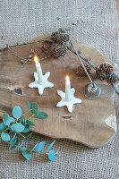 Two burning candles on star-shaped holders on a wooden base