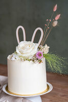 White cake with floral decorations and paper bunny ears
