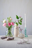 Wooden table with flower arrangement in glass and porcelain vases with twisted candle and linen napkins