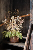 Dried flower arrangement in a brown pot on a wooden staircase