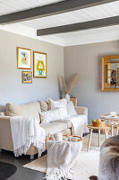 Beige-coloured living room with sofa and wooden tables, gold-framed pictures on the wall