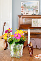 Vase with colourful zinnias on a wooden table, piano in the background