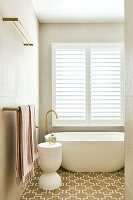 Freestanding bathtub with gold fittings and patterned floor in modern bathroom