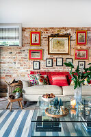 Sofa mit bunten Kissen vor Backsteinwand mit gerahmten Bildern