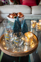 Dekoratives Arrangement mit Mini-Tannenbäumen und Gläsern auf Glastisch