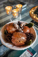 Weihnachtliche Dekoration mit kupferfarbenen Kugeln und Zapfen in Schale auf Glasstisch