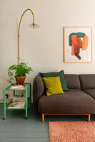 Brown sofa with cushions next to green side table and arc lamp in the living room