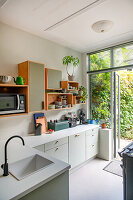 Bright modern kitchen with open wooden shelves and view of the garden