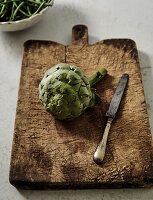 Artischocke auf rustikalem Holzbrett mit altem Messer