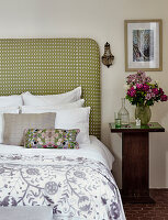 Bett mit grün gemustertem Kopfteil und floralem Kissen im Schlafzimmer
