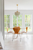 Round dining table with wooden chairs and chandelier in front of large windows