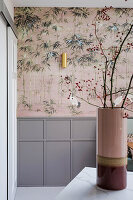 Flur mit Kranich-Tapete, Holzverkleidung in Grau und goldener Wandlampe, Blumenvase mit Zweigen auf Arbeitsplatte aus Marmor