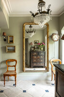 Pastel-coloured wall with antique mirror and two wooden chairs