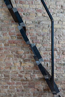 Metal ladder with black railing in front of brick wall