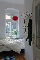 Schlafzimmer mit Fenster, rotem Lampenschirm und bunter Wandgarderobe