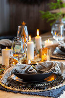Festively laid table with dark crockery, woven placemats and candles