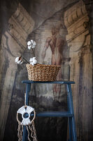 DIY wall decoration and basket with cotton branches on a ladder in front of antique wallpaper