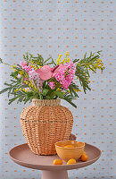 Spring bouquet with flamingo flower (anthurium), hyacinth and mimosa in a woven vase on a round table