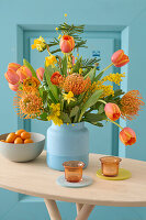 Colourful spring flower bouquet with tulips (Tulipa), pincushions (Leucospermum) and daffodils in a blue vase on a wooden table