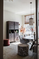 Bright dining room with stylish wooden cabinet and velvet poufs
