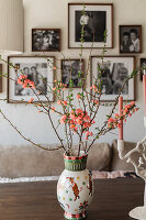 Blossoming cherry branches in a patterned vase on a wooden table in front of framed photos