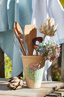 Holz-Küchenutensilien und Hortensien in Tontopf auf Holztisch im Garten