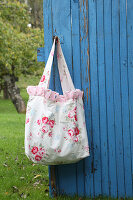 Self-sewn bag with rose pattern and ruffles on blue wooden door in the garden
