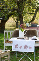 Autumnal table runner with leaf print on a small table in the garden