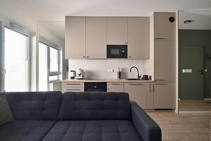 Modern fitted kitchen with black accents and grey sofa in the foreground