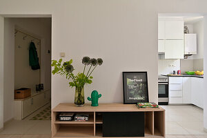 Wooden shelf with decorative elements in front of open-plan kitchen/living room