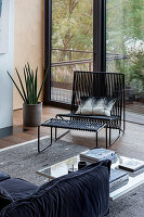 Modern seating area with black wire armchair and matching stool in front of large window front