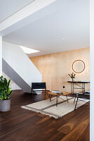 Minimalistisches Wohnzimmer mit heller Holzwand, schwarzem Ledermobiliar und Pflanzenakzenten