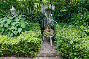 White metal chair with wreath of flowers between boxwood hedges in the garden