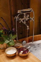 Herbal mixtures and bath salts next to wooden bathtub with chrome-coloured retro fittings