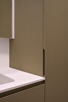 Detail of a modern fitted kitchen with handleless cabinets in olive tones