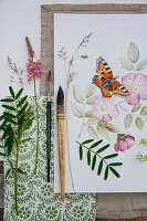 Watercolour painting of a small fox on a wild rose blossom with painting utensils